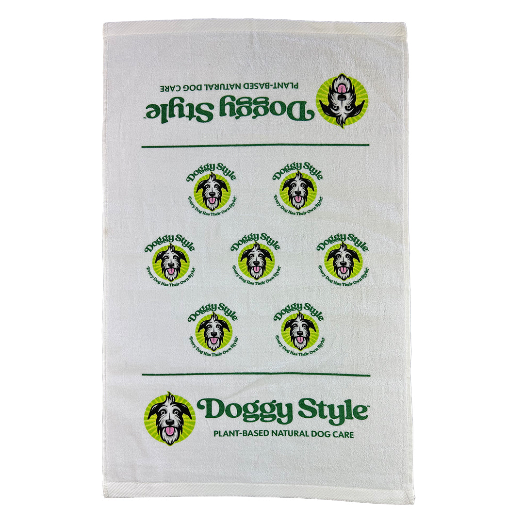 A white pet towel with green and black text and graphics, including the logo 'Doggy Style' and images of dogs' heads.